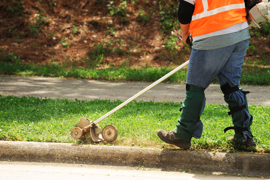 A lawn maintenance worker using an edger to edge a sidewalk